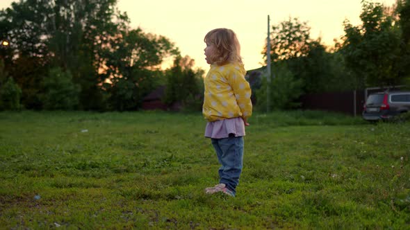 Curly Blonde Girl Child Stands in Field Alone at Sunset and Looks Ahead