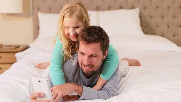 Daughter lying on father using mobile on bed in the bedroom