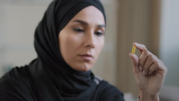 Young Female Thoughtful Patient Arabian Islamic Girl in Hijab Hold Yellow Medicine Capsule Vitamin