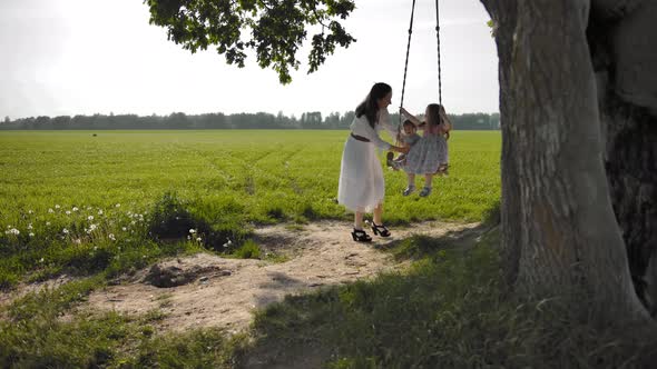 A Young Woman Is Swinging on a Swing Two of Her Children 1 and 3 Years Old