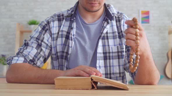 Close Up of a Young Man with a Rosary in His Hands Reading the Bible