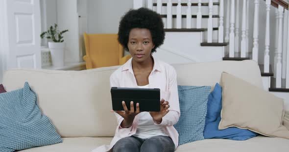 Black Woman with African Hairstyle Working on Tablet PC, Sitting on Comfortable Couch