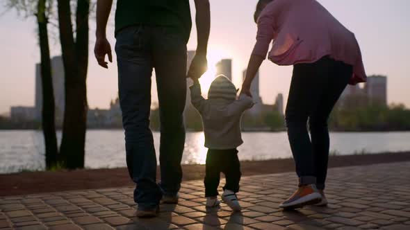 Young Mother and Father Teach the Child to Walk Along the Path