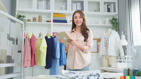 Portrait of Asian tailor woman designer smile and look at camera after success in make new dress