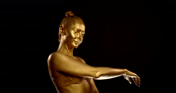 a Girl with Golden Glowing Skin and Lingerie Posing on a Black Background. She Closed Her Eyes