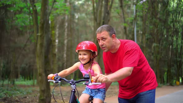 Closeup. Portrait of a little girl. Her dad is teaching her to ride a bike. Happy girl.