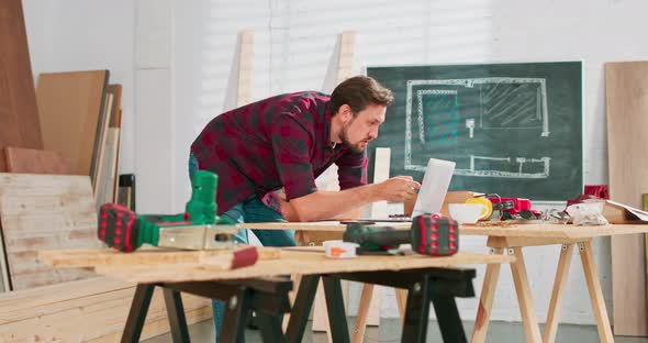 Portrait of Modern Young Bearded Man Speaking By Phone with Client Smiling and Making Notes in