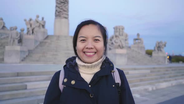 Front view of Asian woman standing and looking at camera in public Frogner park, Norway