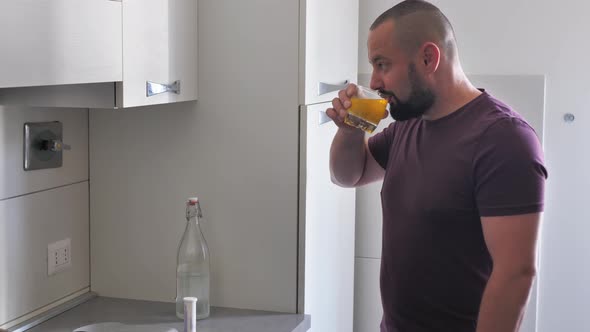 Bearded Man in the Kitchen Drinks Vitamins or Orange Juice