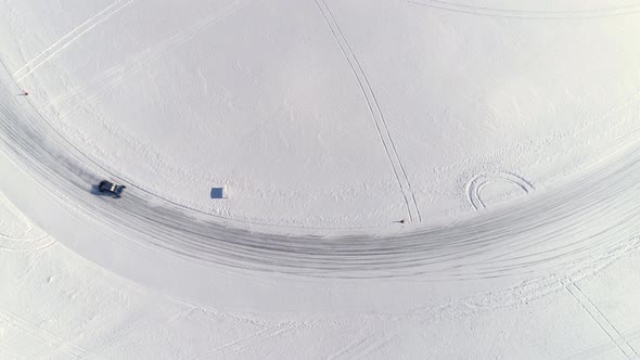 Observed from high above, a custom built utility vehicle drifts around an icy corner on a frozen rac