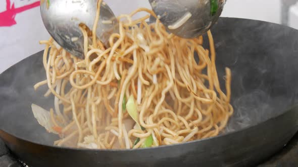 A Female Cook's Hand Frying a Plate of Thai Noodles in a Frying Pan at an Outdoor Food Festival