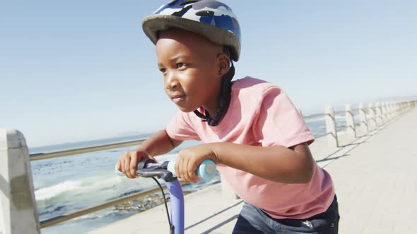 Video of happy african american boy riding scooter by sea