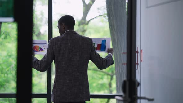 Back View of Overwhelmed African American Young Man in Suit Throwing Paperwork Putting Hands on Hips