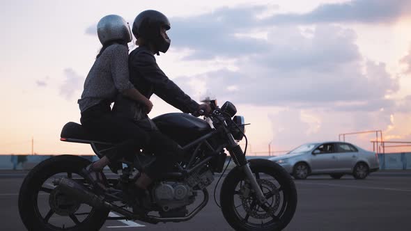 Young Couple in Helmets Riding on Motorcycle in City with Beautiful Sunset Sky Background Slow