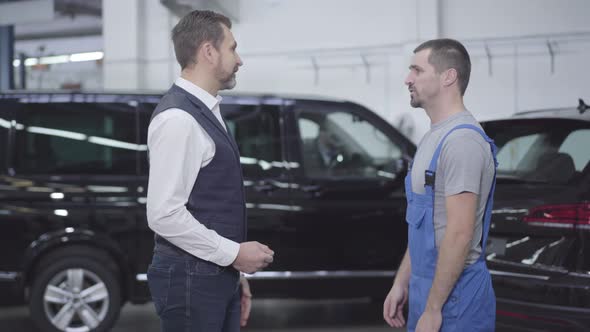 Side View of Two Caucasian Men Standing in Auto Repair Shop and Talking. Successful Businessman