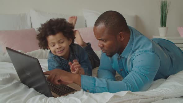 African Father and Son Networking with Laptop on Bed