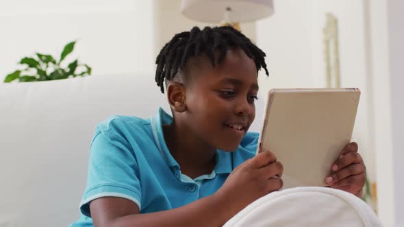 African american boy smiling while using digital tablet sitting on the couch at home