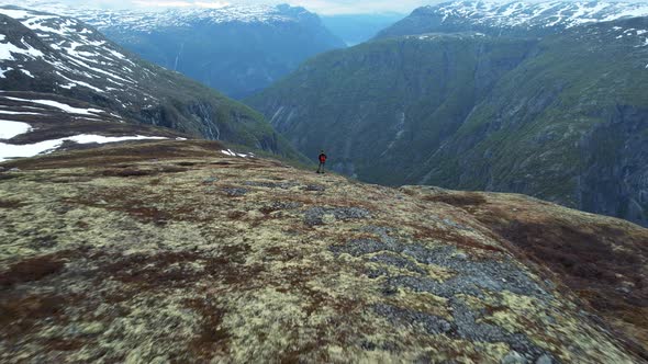 Aerial View Of Lone Adult Male Standing On Edge Top Of Voringsfoss In Norway. Dolly Back, Rising Sho