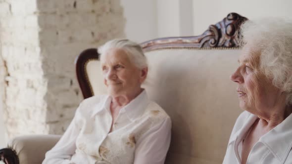 Two Cute Grandmothers Sitting on a Sofa and Talking Among Themselves in Room