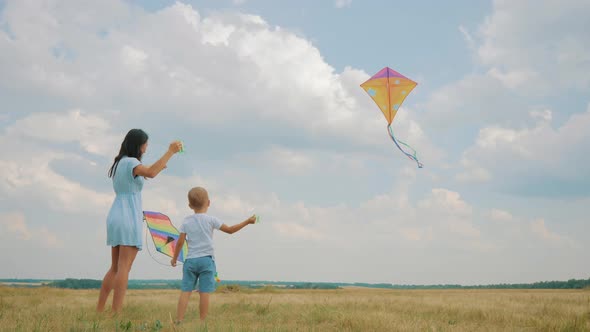 Happy Family Mom and Son Playing with Flying Kite on Meadow in Beautiful Sunny Day Blue Sky