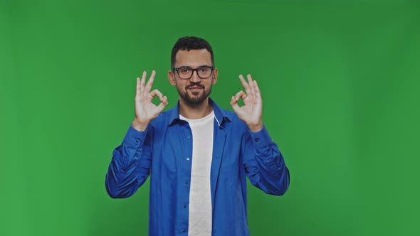 Smiling Handsome Man Wearing Casual Clothes Showing Ok Sign Gesture at the Camera Over Green