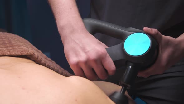 Closeup Percussion Massager in the Hands of a Masseur Makes a Massage of the Shoulders and Upper