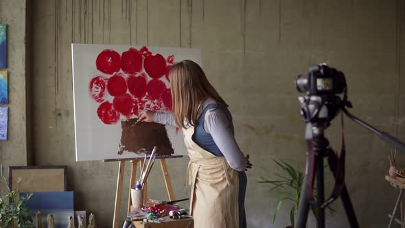 Female Caucasian Mature Blogger Recording Video in Workshop Drawing Pink Flower on Canvas Explaining