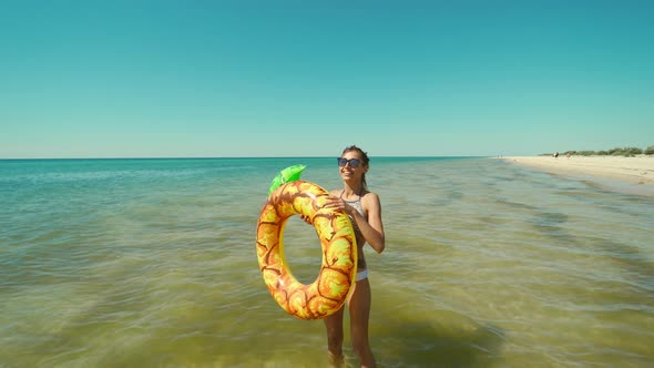 Portrait of Happy Smiling Young Woman in Sunglasses with Inflatable Pineapple Standing in Sea Water