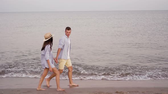 A Young Beautiful Couple is Walking Along the Sea or Ocean a Man and a Woman Dressed in Shirts