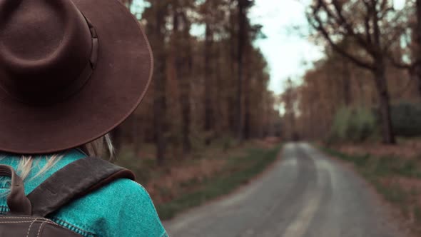 Woman with backpack walking on road in forest in spring time