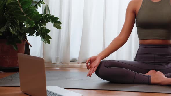 Asian woman practicing yoga from yoga online course on a video conference on a laptop at home.