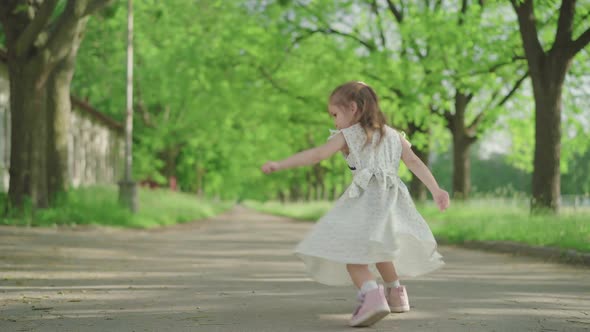 Cheerful Caucasian Girl Spinning and Jumping in Sunny Summer Park. Wide Shot Portrait of Pretty