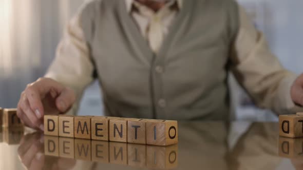 Old Man Making Word Dementia of Wooden Cubes on Table, Brain Disease, Health