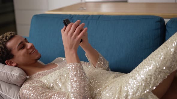 Cheerful Guy in Fancy Dress Using Mobile Phone Laying on Sofa