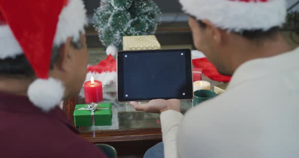 Father and biracial son making christmas video call on tablet pc with blank screen and copy space