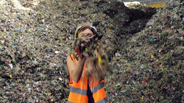 Young Woman in Protective Gear Blows Litter at you at City Trash Dump