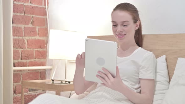 Focused Redhead Young Woman Using Tablet in Bed