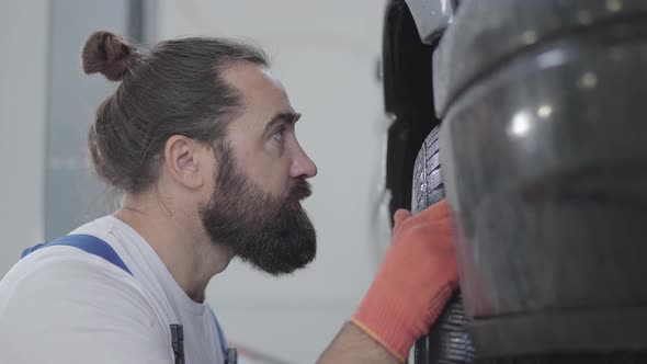 Portrait Bearded Professional Mechanic Inspecting Suspension or Brakes in Car Wheel