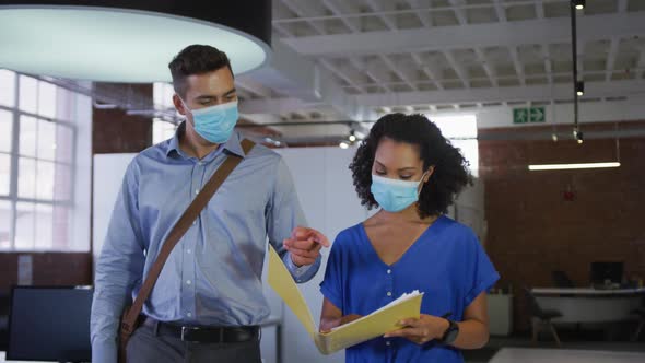 Diverse race male and female businessmen walking discussing through corridor wearing facemask