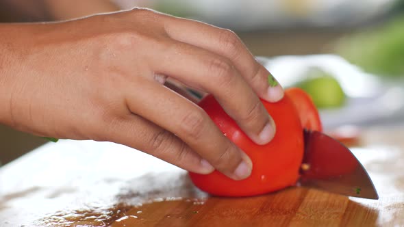 Macro Shot on Woman's Hand Slicing a Ripe Tomato on a Wooden Chopping Board.