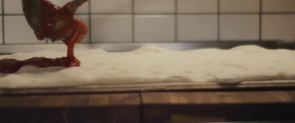 Tomato sauce being spread over a fresh pizza dough. Close up, super slow motion.