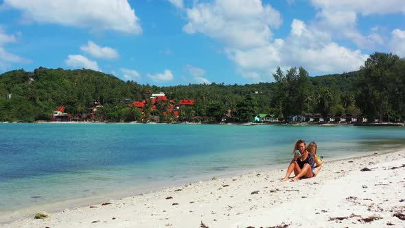 Women sunbathing on tropical tourist beach trip by blue green sea with bright sandy background of Th