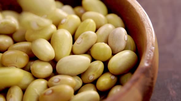 Uncooked peruvian bean fall into a wooden bowl. Falling mayocoba grains. Macro. Canary legumes