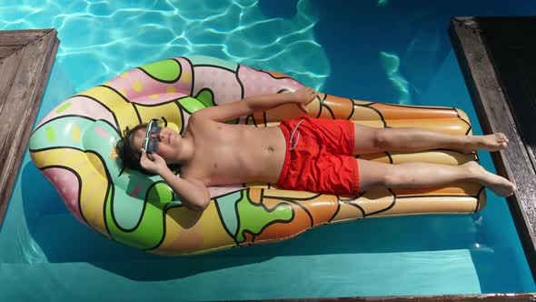 Top View of Relaxed Little Boy in Sunglasses Lying on Swimming Mattress Sunbathing in Swimming Pool