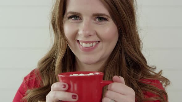 Woman smiling as she raises mug of hot chocolate with marshmallow