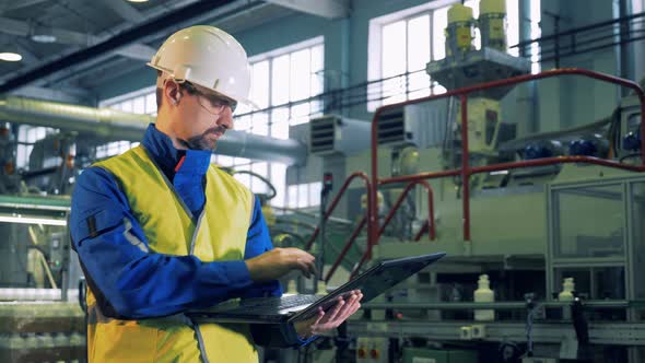 Male Specialist Is Working on a Laptop in a Facility of a Plastic Plant