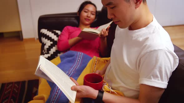 Couple relaxing on sofa reading book in living room