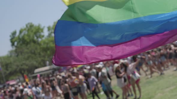 The LGBTQ rainbow flag waving in slow motion with people in a pride parade in the background