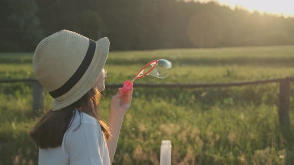 Beautiful Child Girl in a Hat Blowing Soap Bubbles