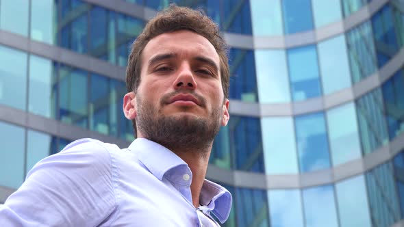 A Young Handsome Man Looks at the Camera in an Urban Area - Closeup From Below - an Office Building